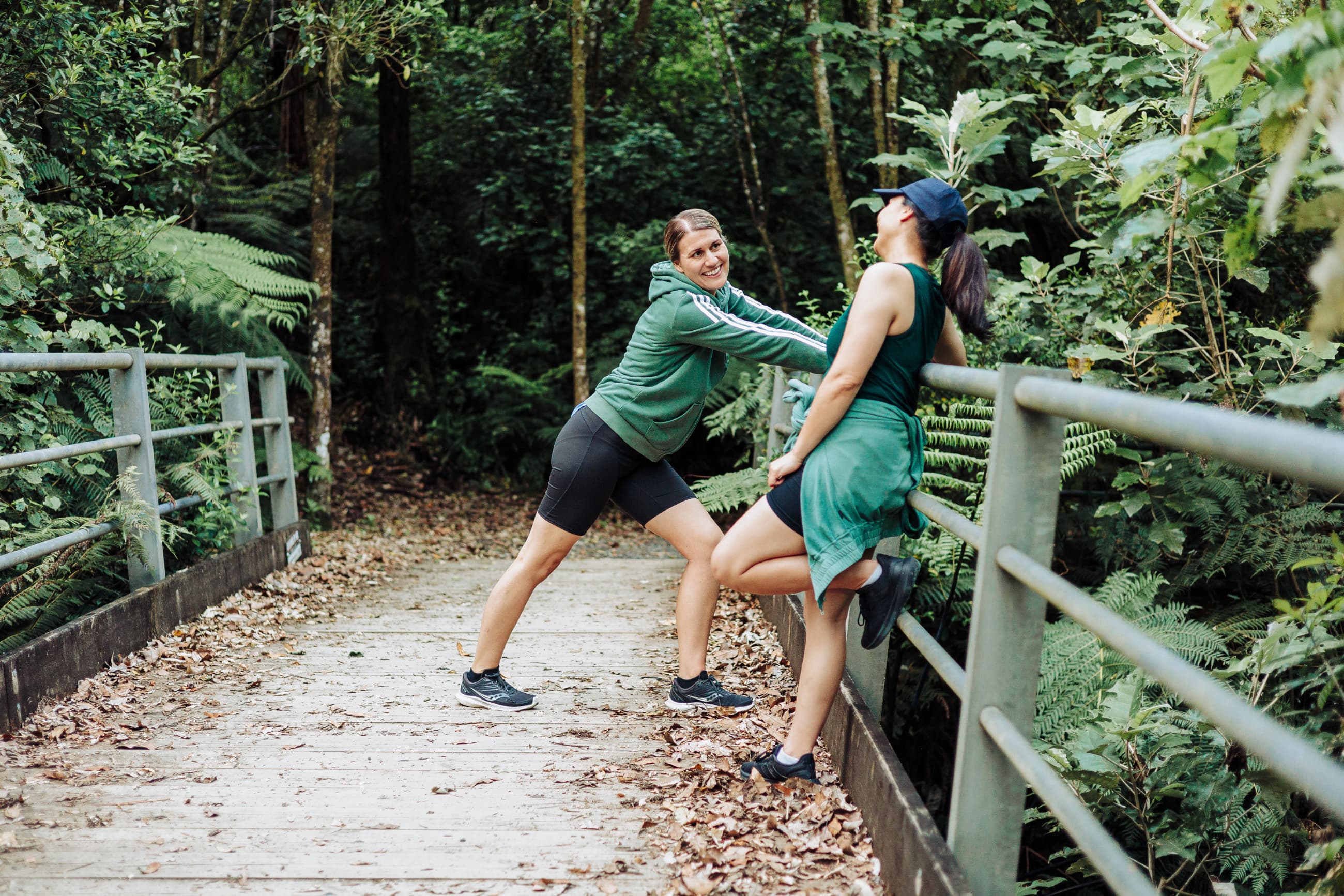 Two women stretching together on a bush walkway in Aotearoa